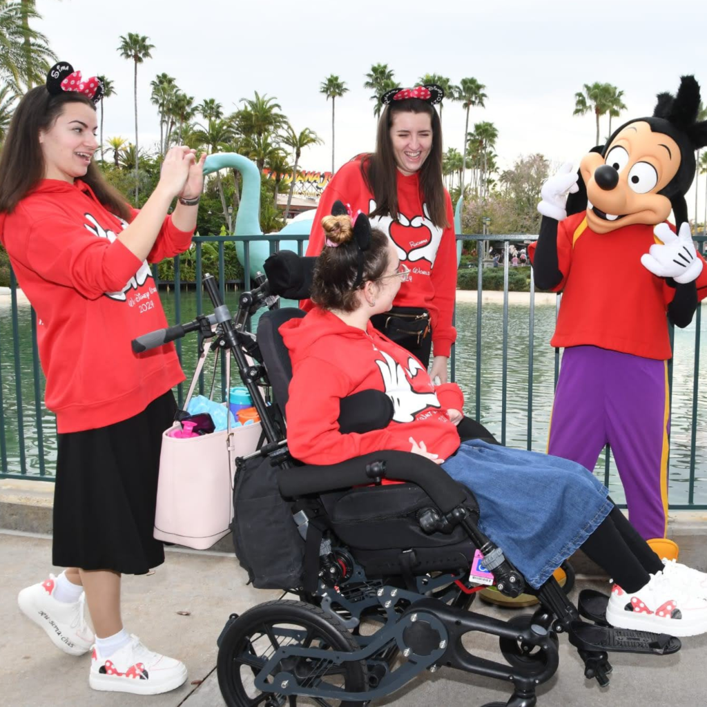 Chasya seated in her Chunc One chair at Disneyland with Goofy and two friends, smiling during a character meet and greet